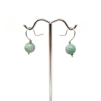 Two light blue pearl earrings with silver hooks on a stand.