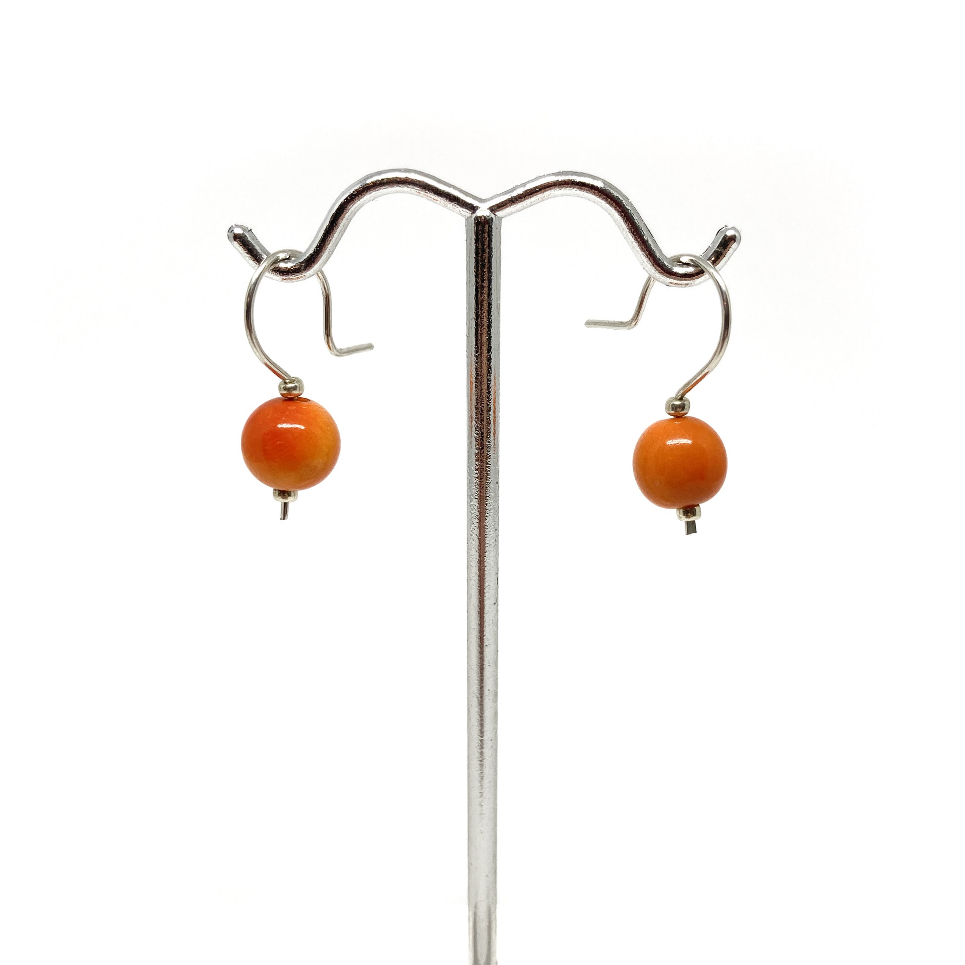 Two orange pearl earrings with silver hooks on a stand.