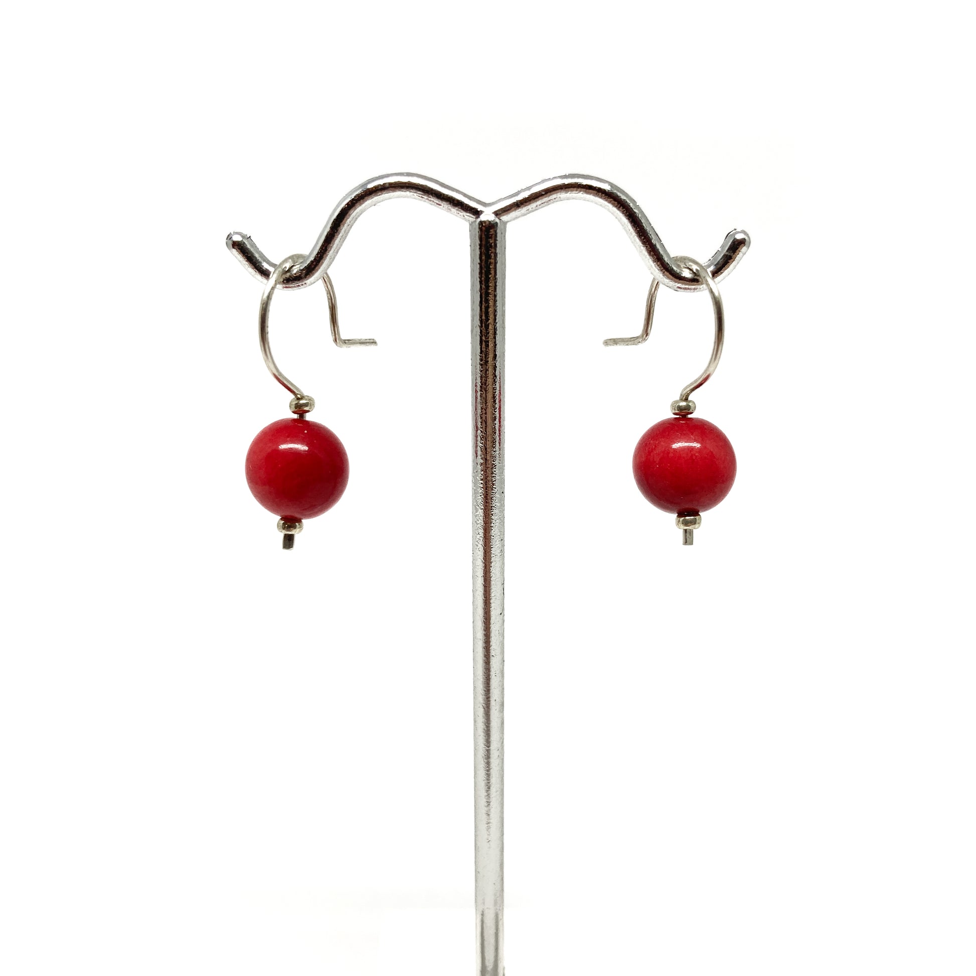 Two red pearl earrings with silver hooks on a stand.