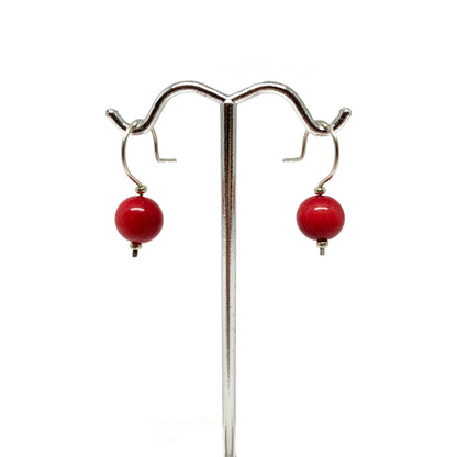 Two red pearl earrings with silver hooks on a stand.