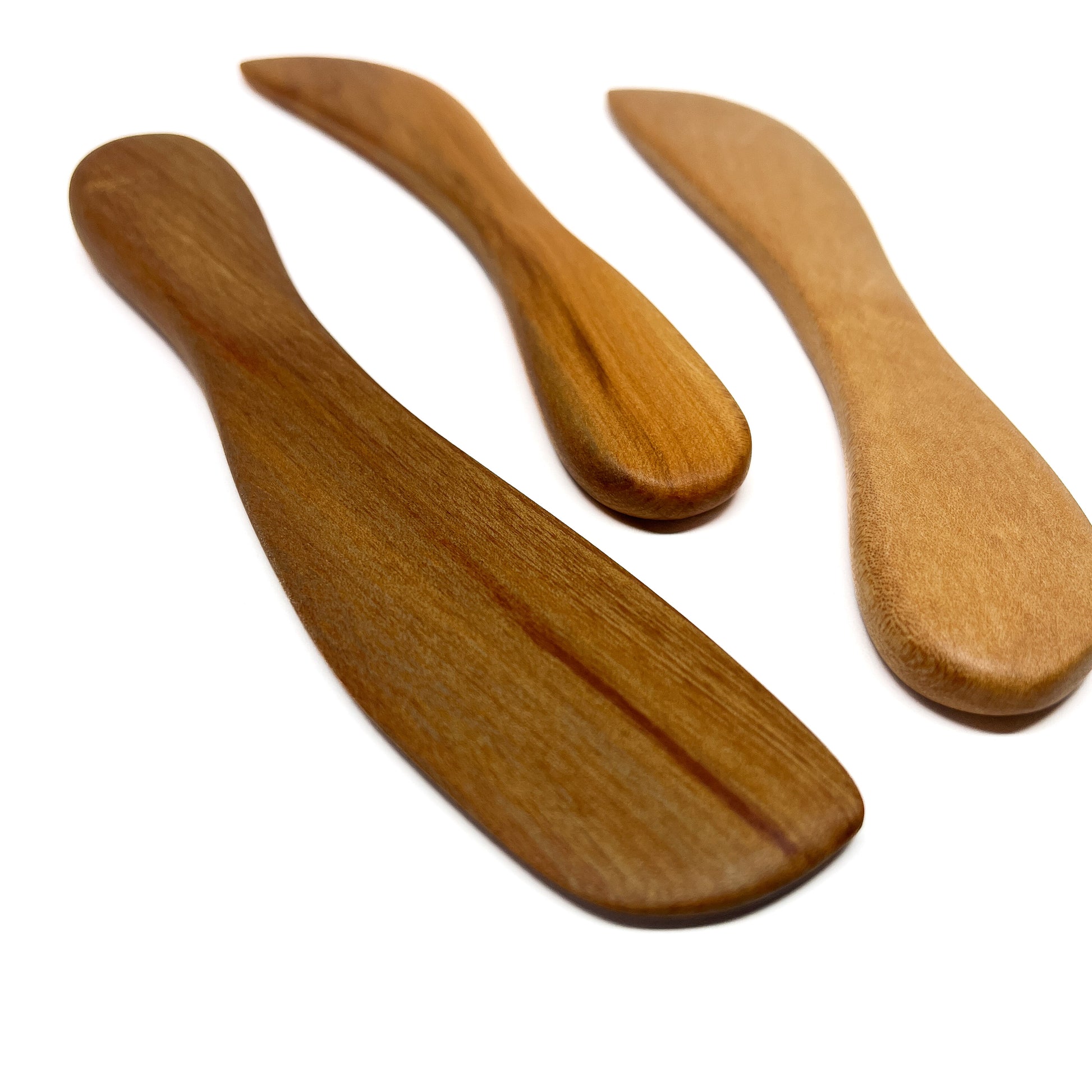 Three wooden spread knives in varying shades, angled on a white surface.
