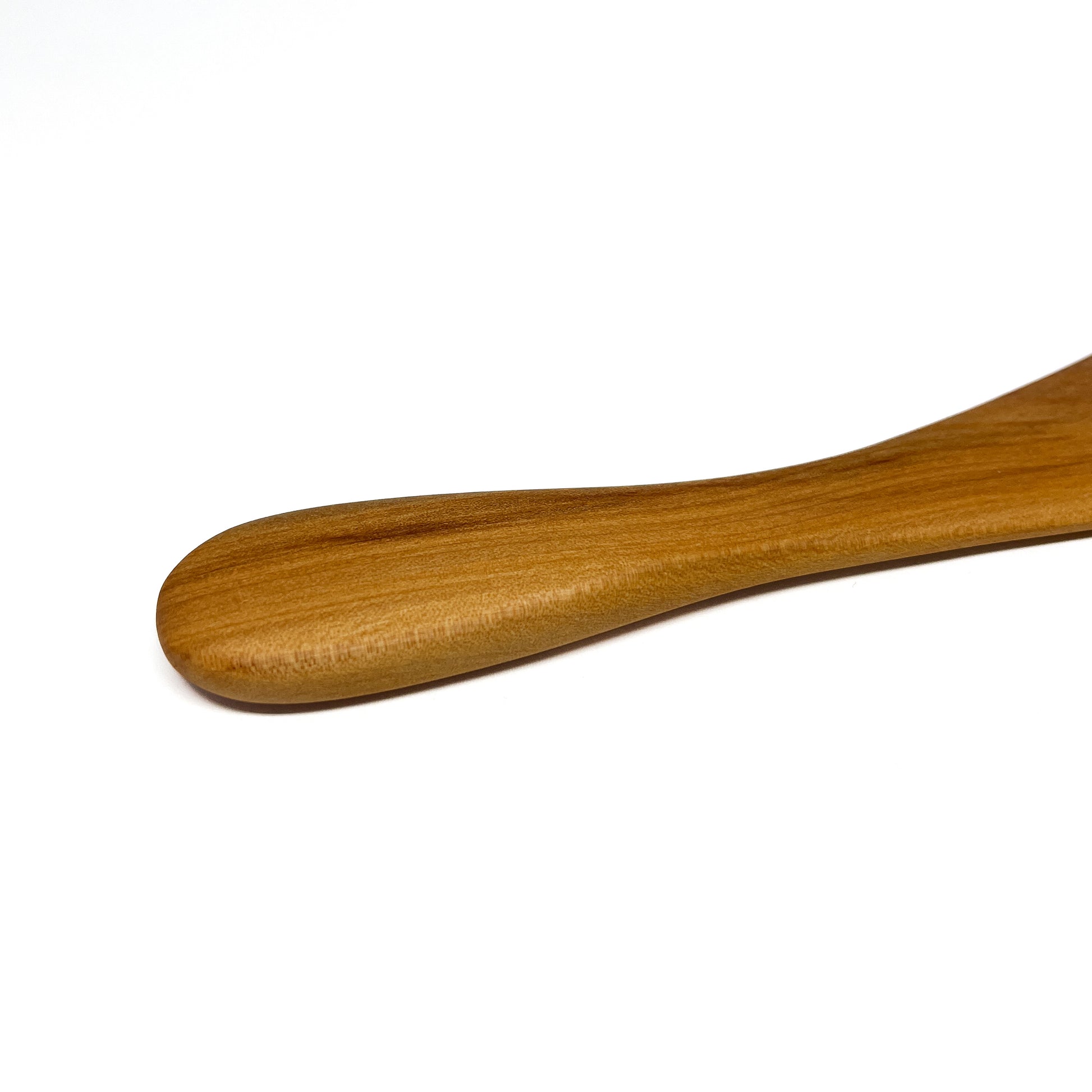Close-up of a wooden spread knife tip, angled on a white surface.