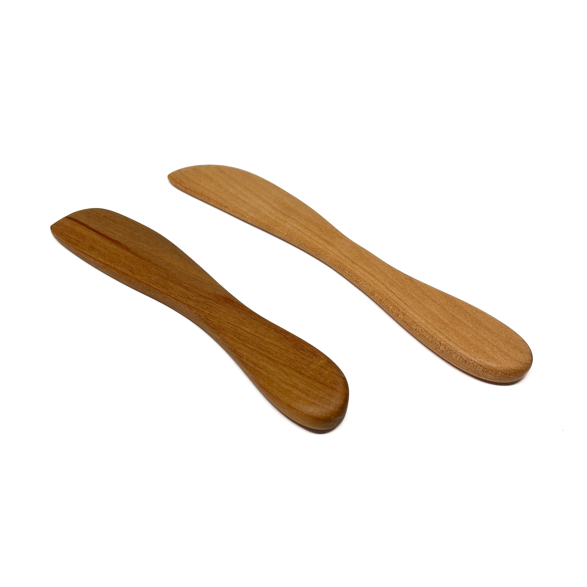 Two wooden spread knives in varying shades, angled on a white surface.