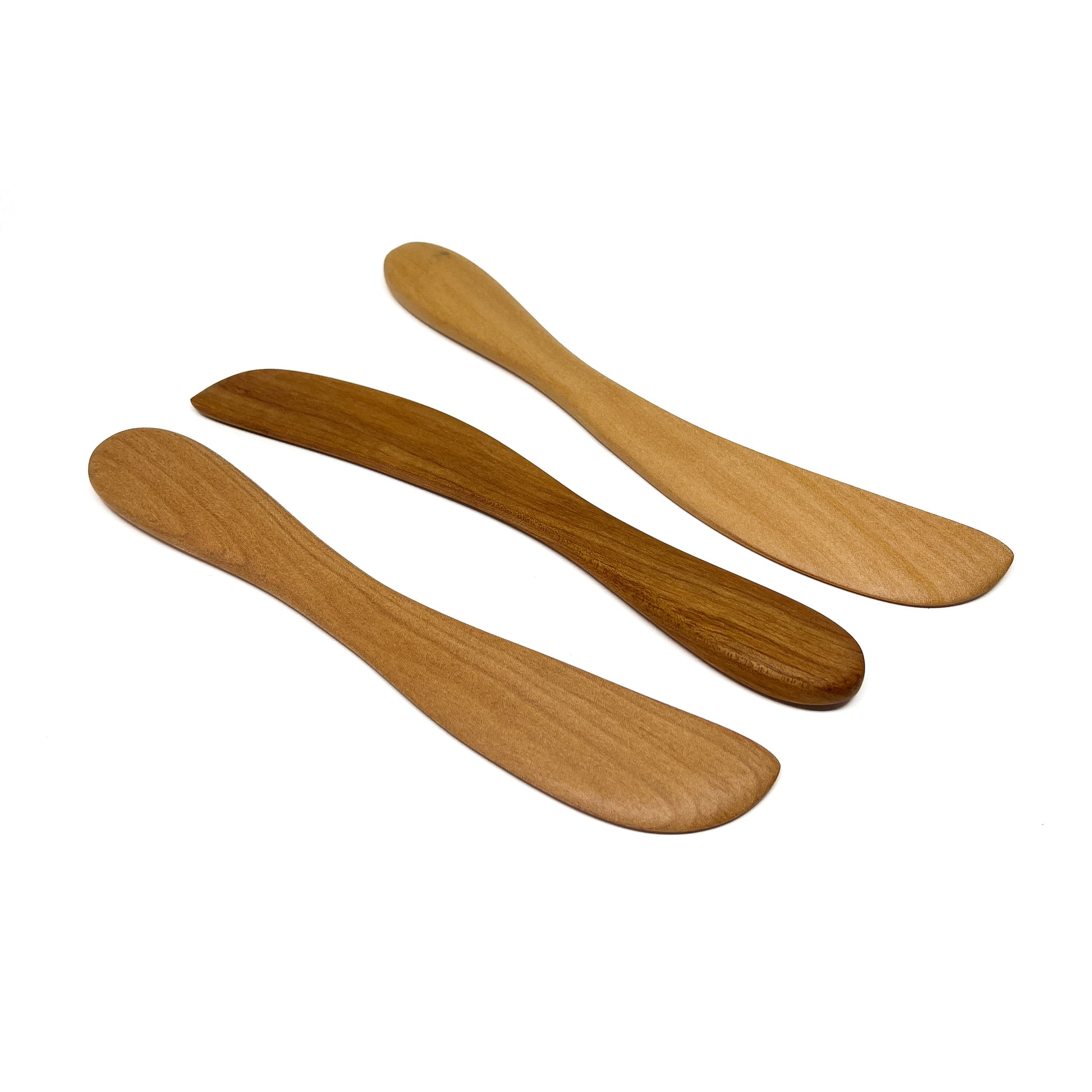 Three wooden spread knives in varying shades, angled on a white surface.