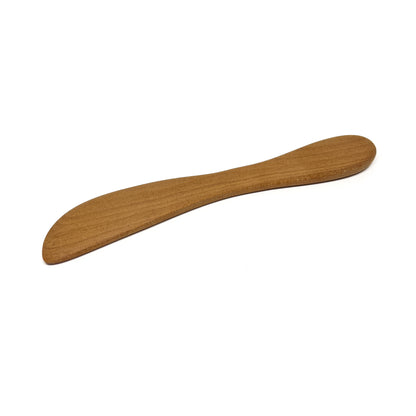 A wooden spread knife, angled on a white surface.