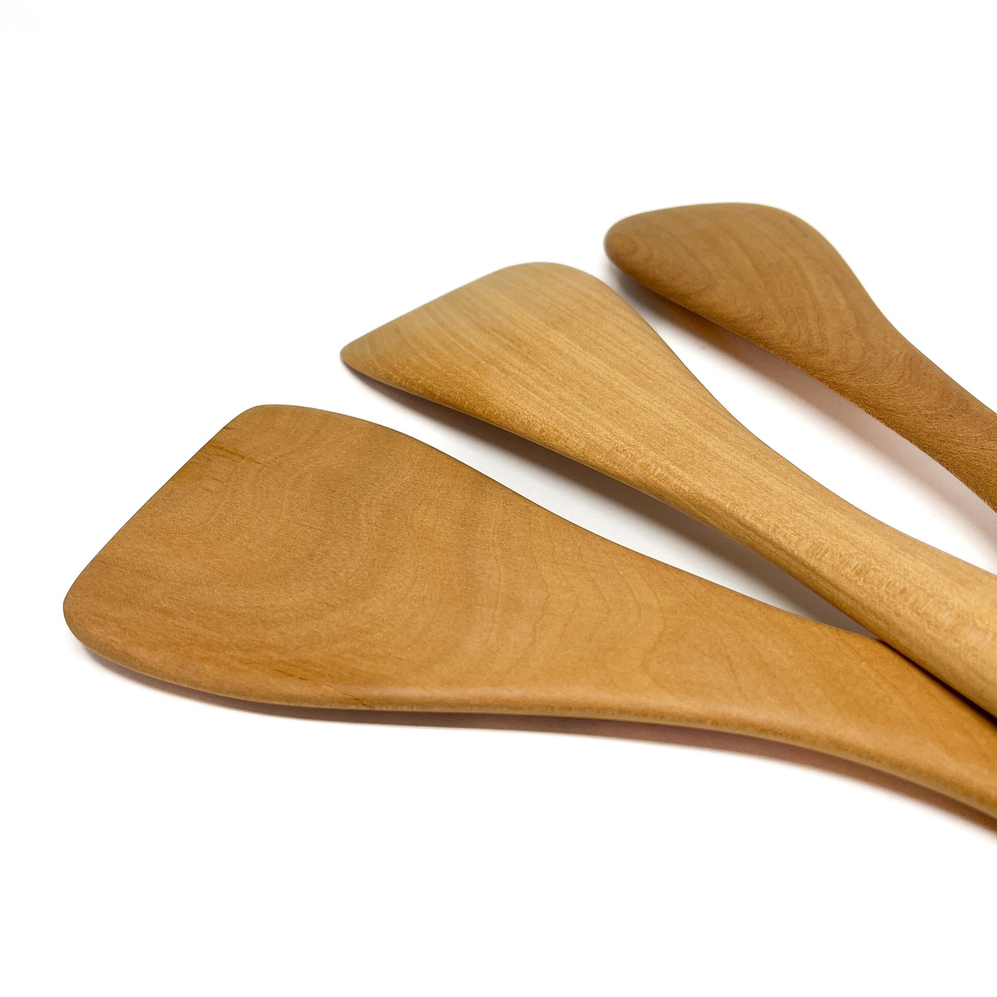 Three wooden spatulas in varying shades, angled on a white surface.