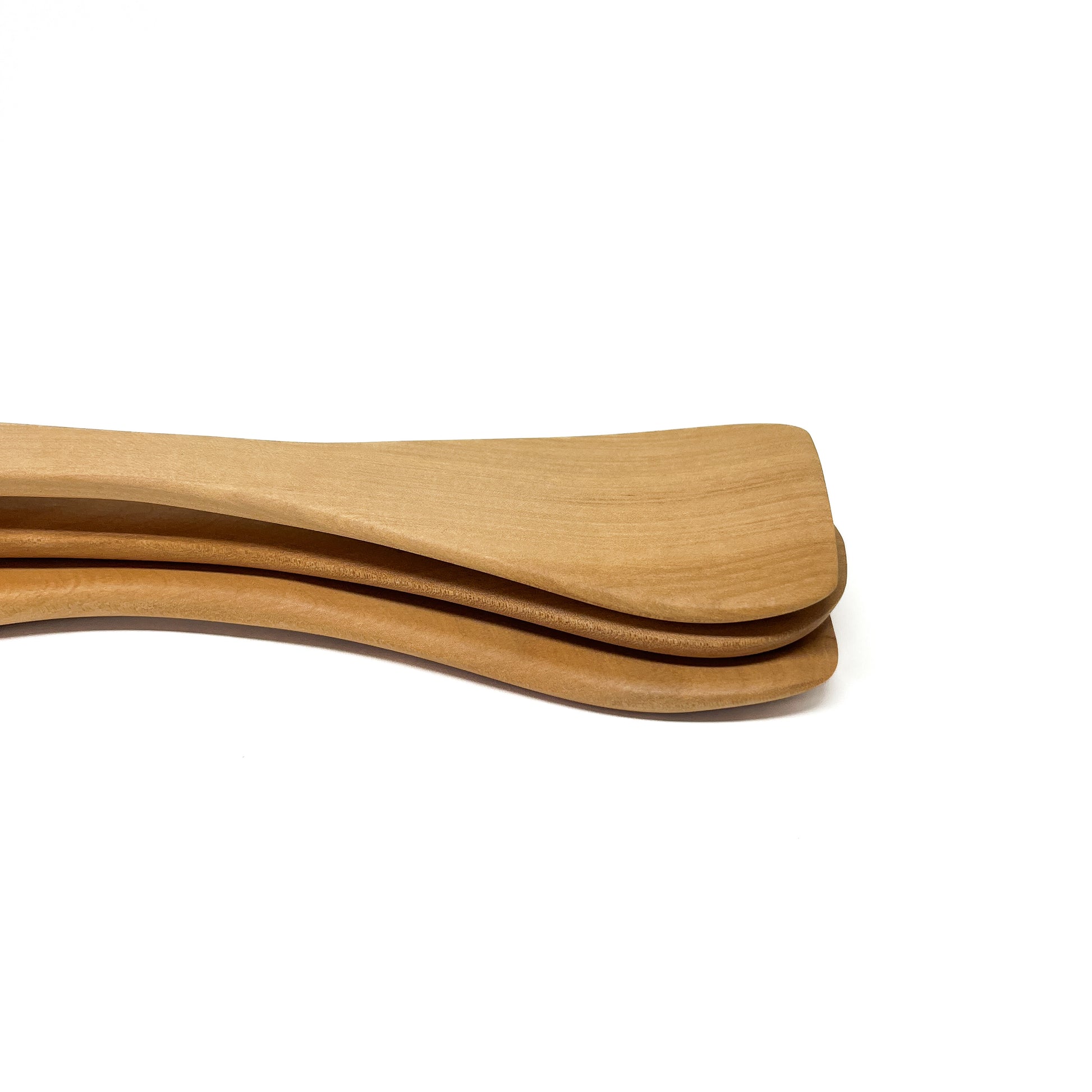 Stacked wooden spatulas in varying shades, angled on a white surface.