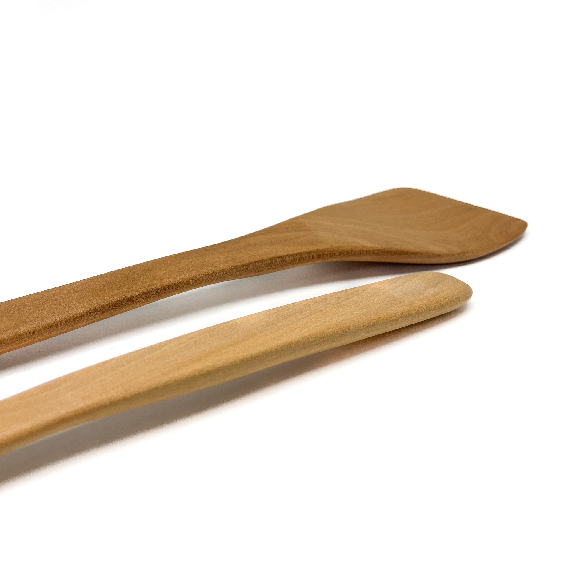 Close-up of two wooden spatulas in varying shades, angled on a white surface.