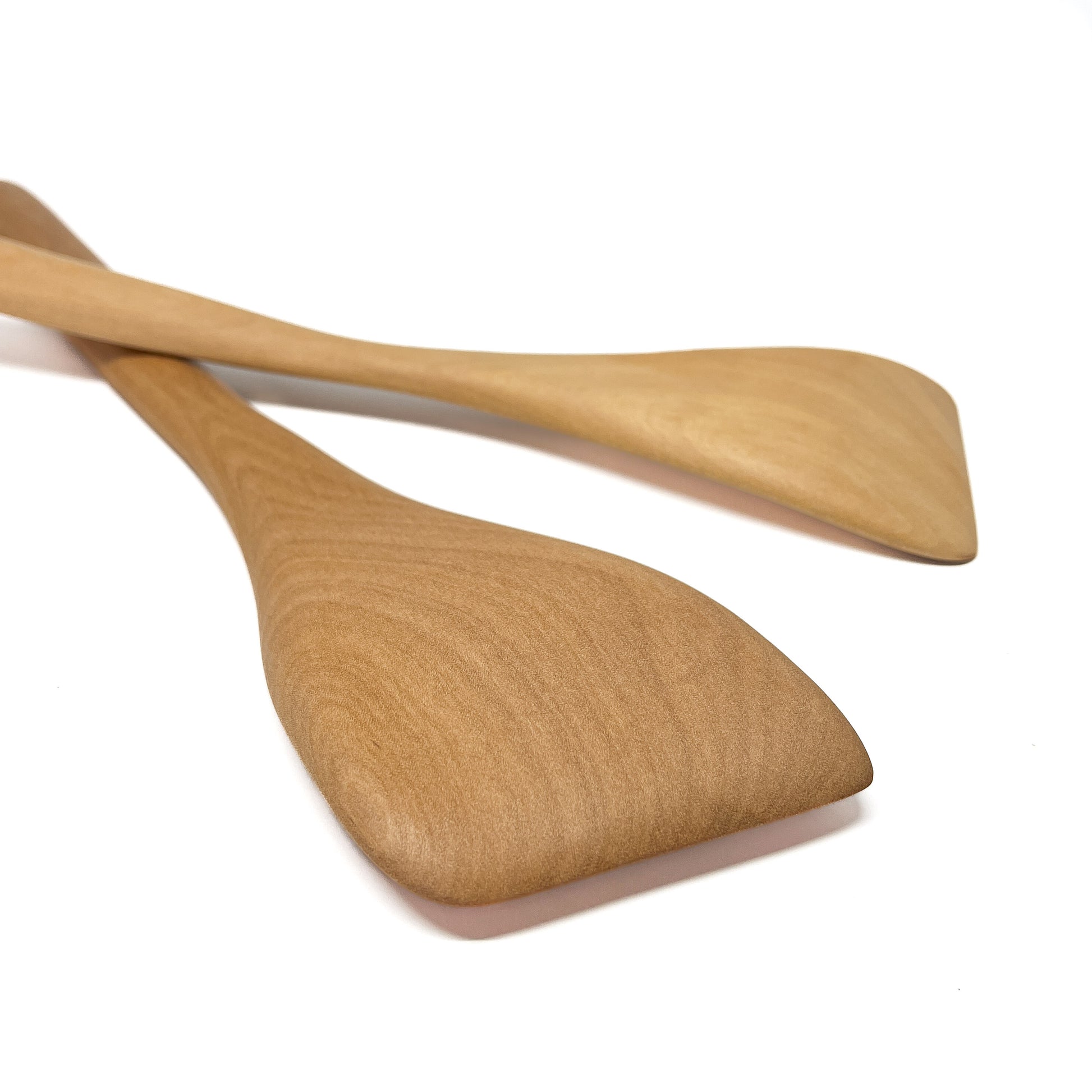 Two wooden spatulas crossed on a white surface.