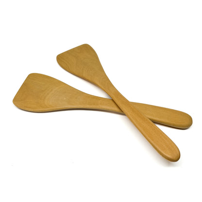 Two wooden spatulas crossed on a white surface.