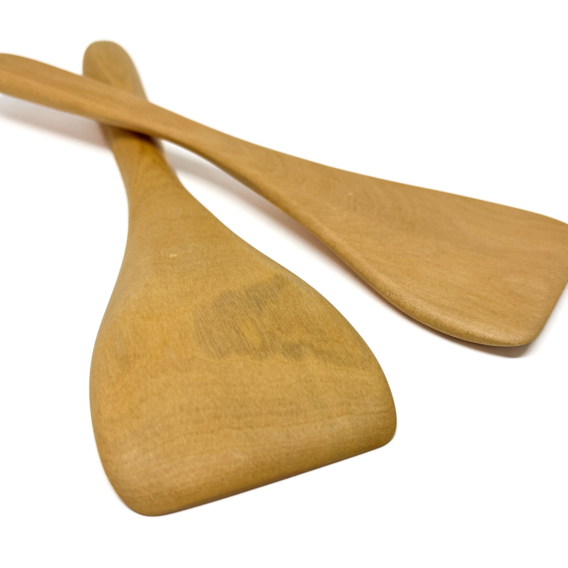 Two wooden spatulas crossed on a white surface.