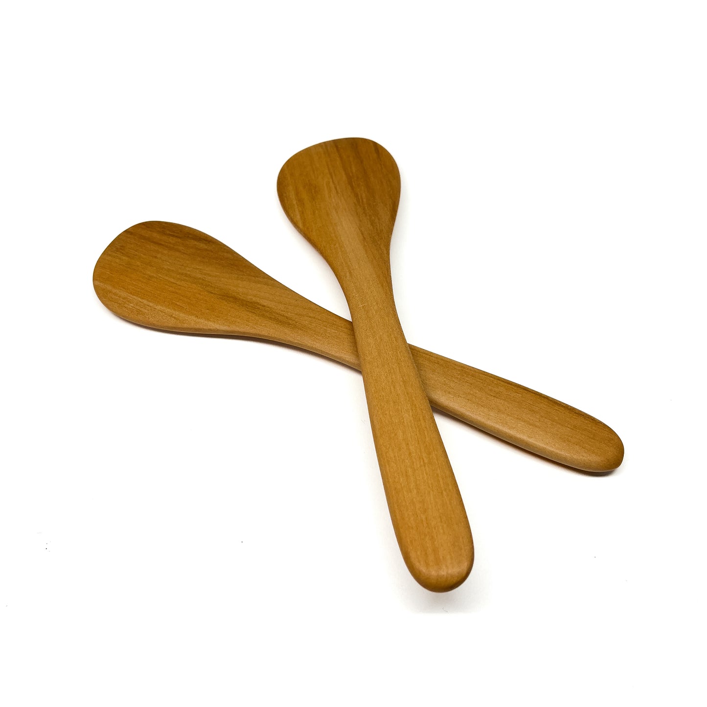 Two wooden spatulas crossed on a white surface.