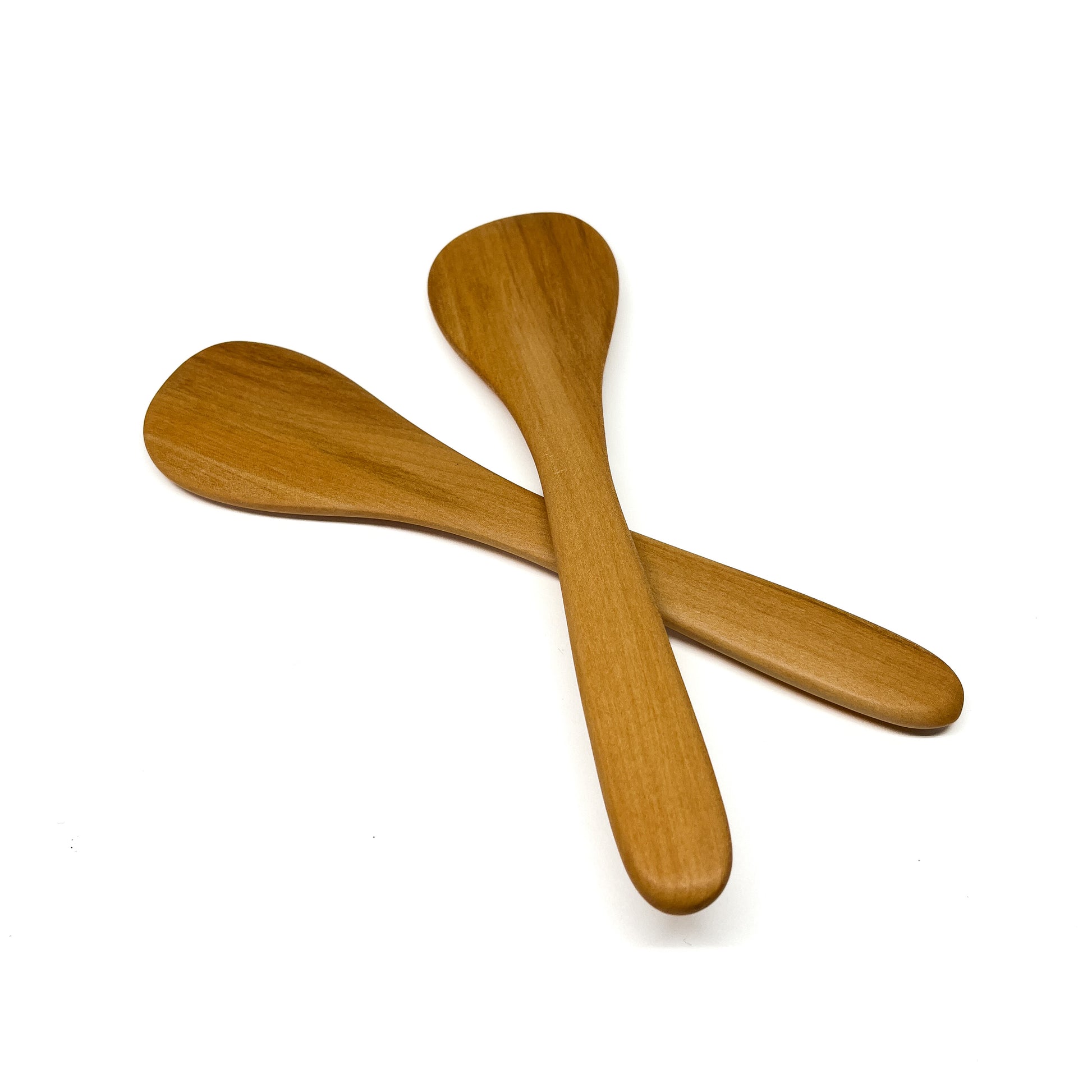 Two wooden spatulas crossed on a white surface.