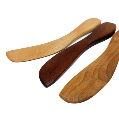 Three wooden spread knives in varying shades, angled on a white surface.