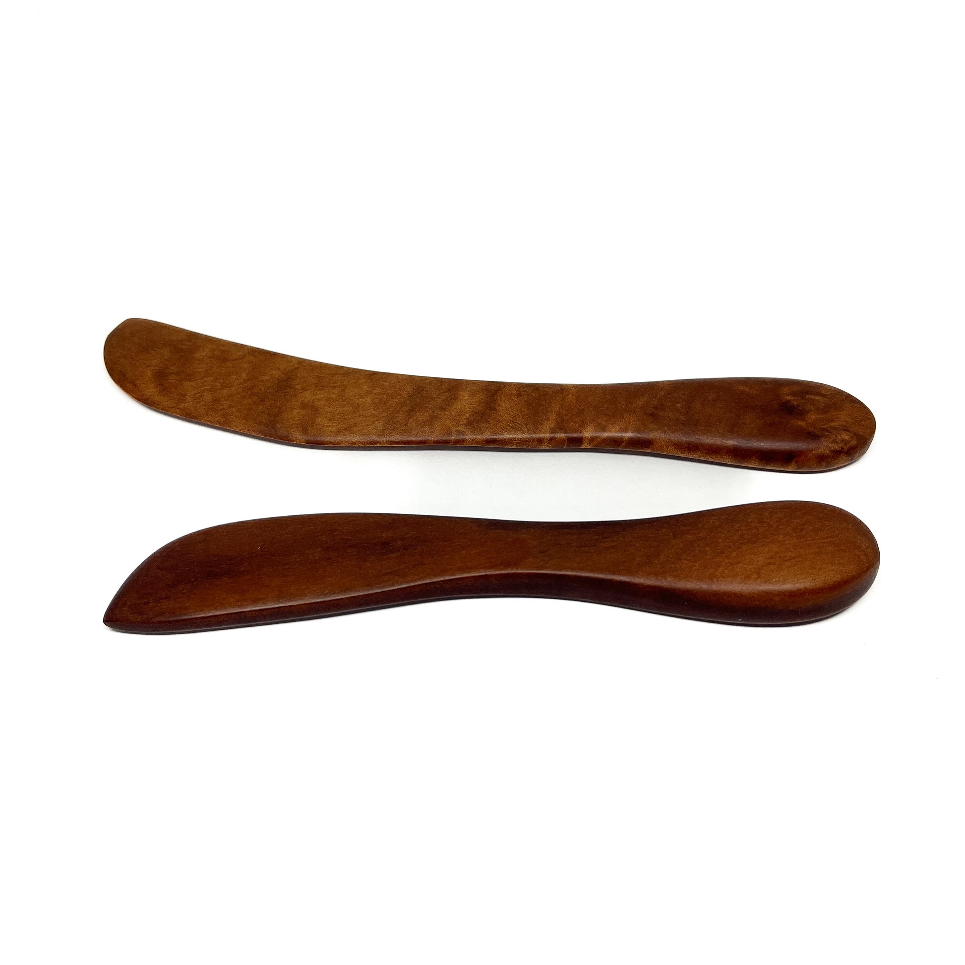 Two wooden spread knives in varying shades, angled on a white surface.