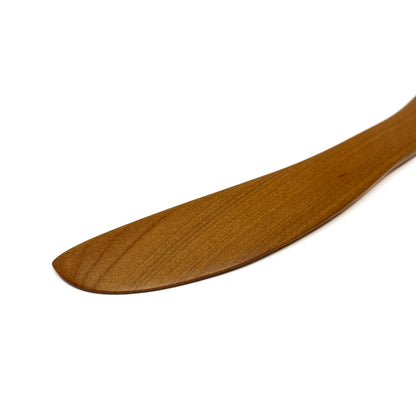 Close-up of a wooden spread knife tip, angled on a white surface.
