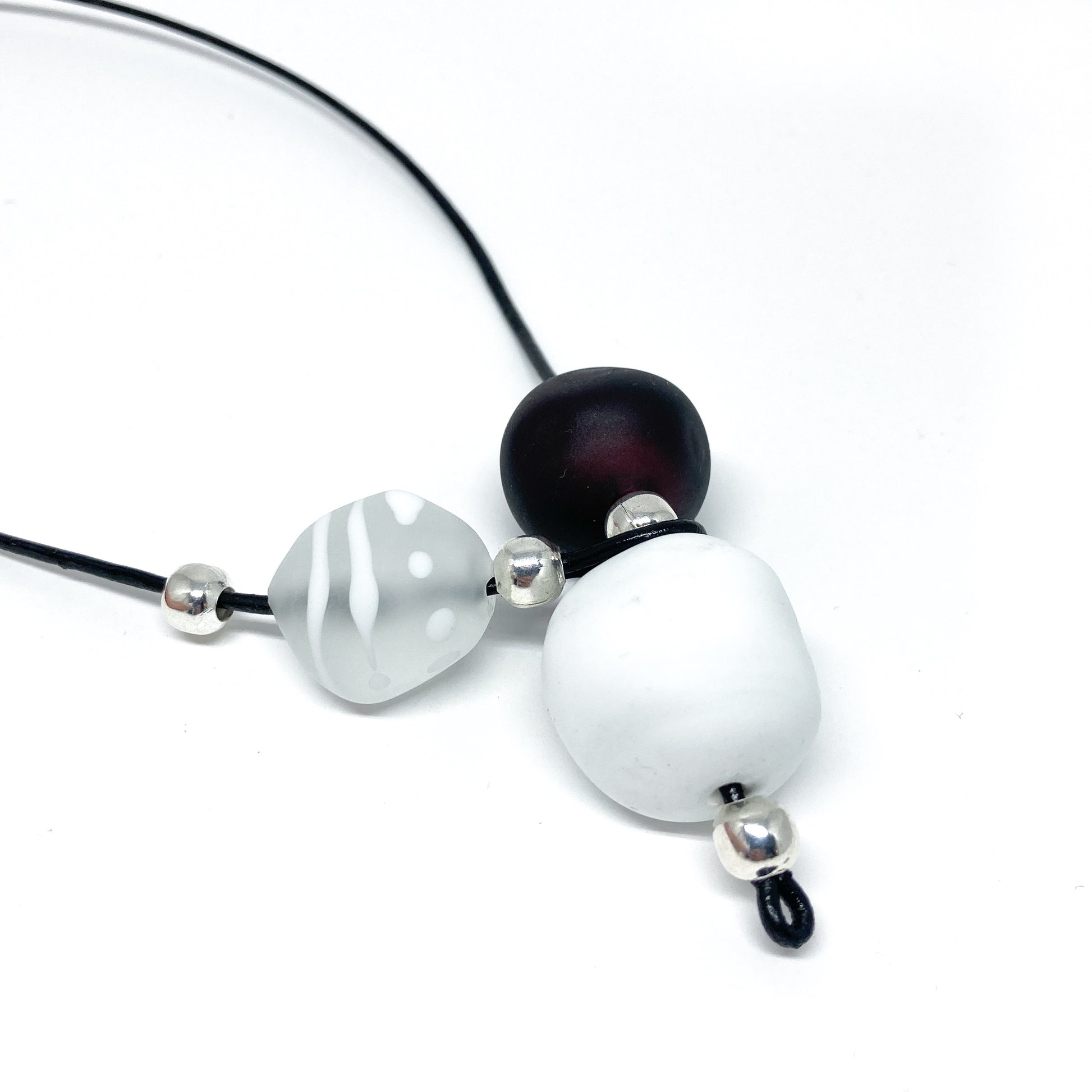 Black cord necklace with white, patterned, and dark beads, and silver accents.