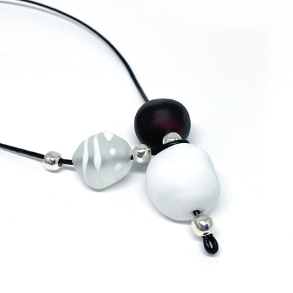 Black cord necklace with white, patterned, and dark beads, and silver accents.