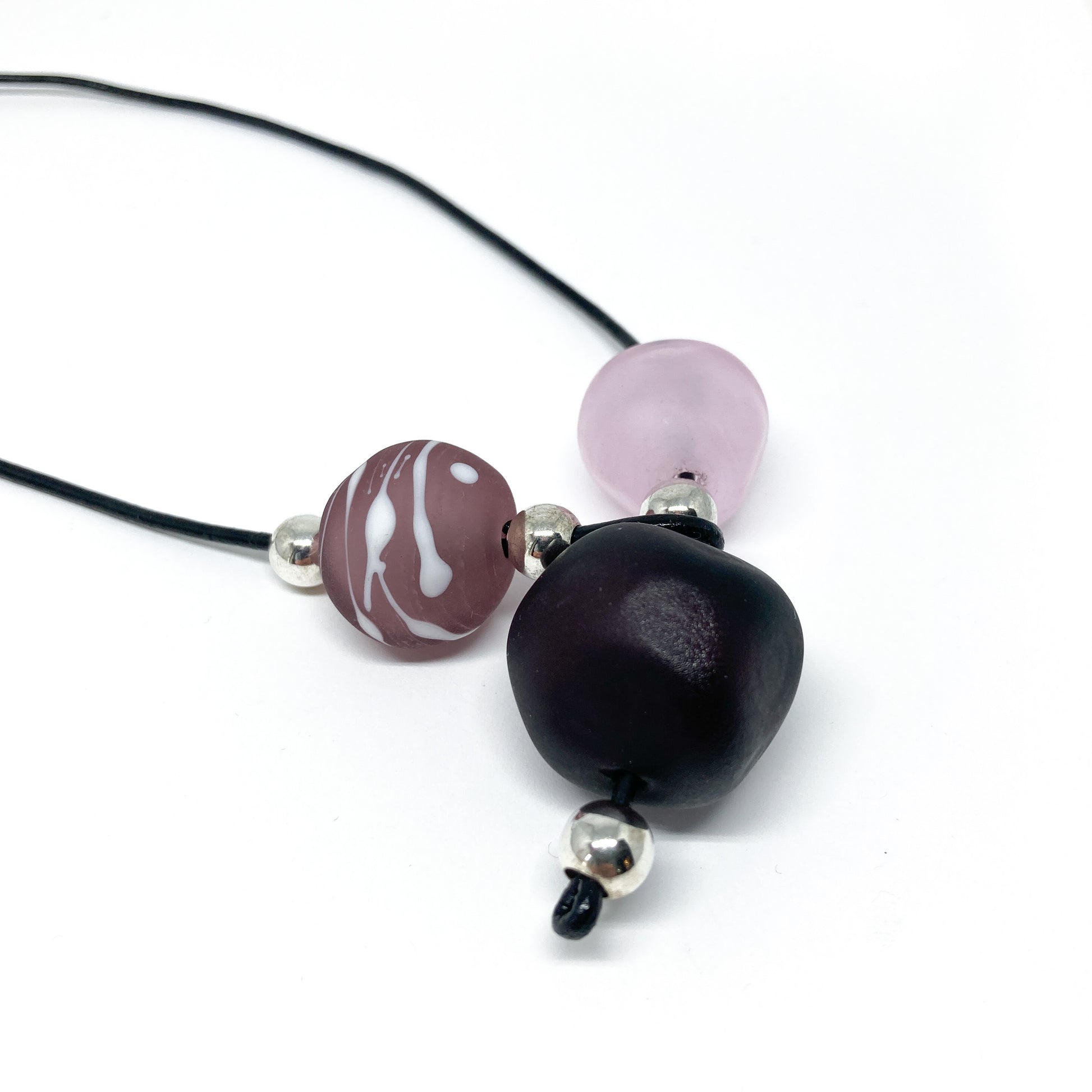 Black cord necklace with purple patterned, dark, and light pink beads, and silver accents.