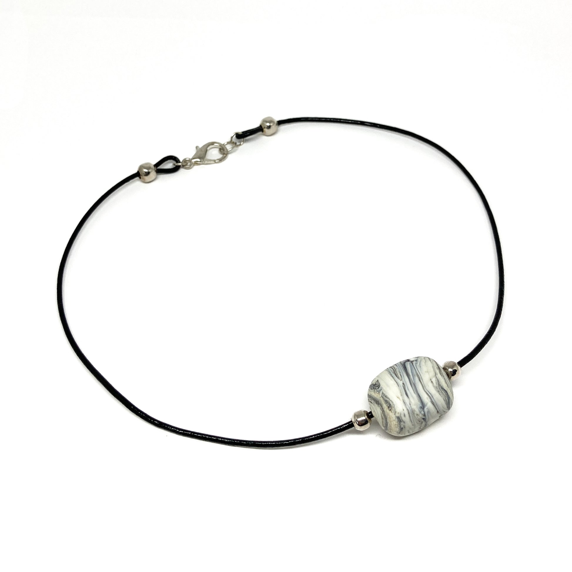 Black cord necklace with a gray striped bead and silver accents, displayed on a flat surface.