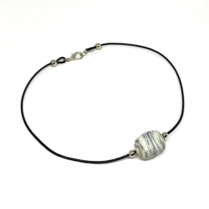 Black cord necklace with a gray striped bead and silver accents, displayed on a flat surface.