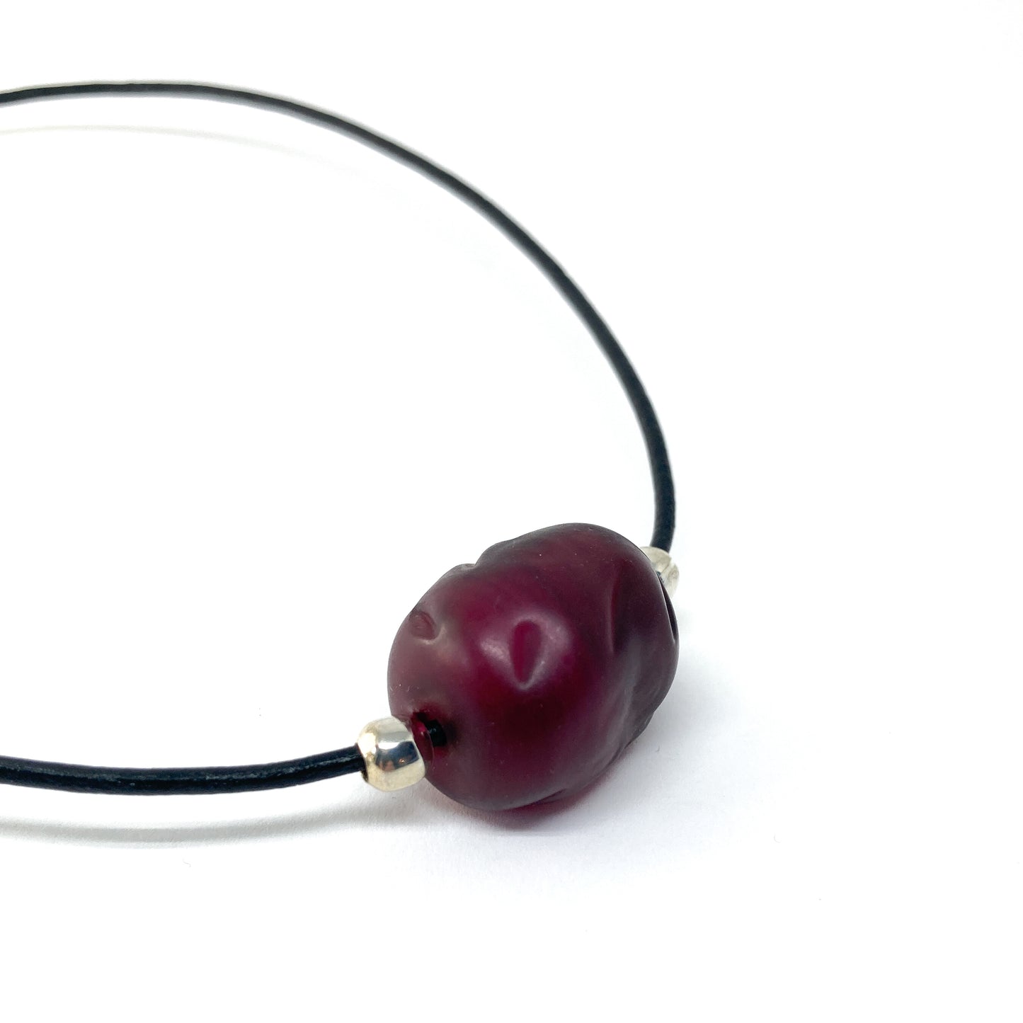 Black cord necklace with a dark red bead and silver accents.