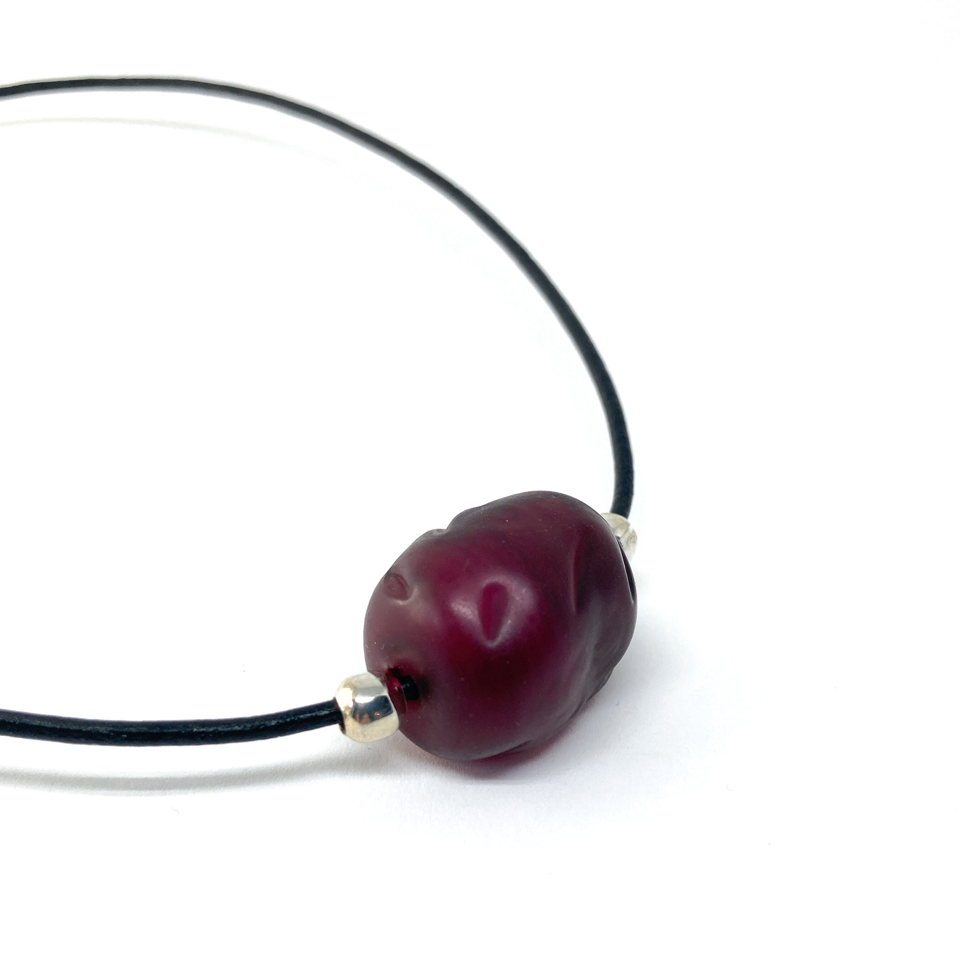 Black cord necklace with a dark red bead and silver accents.