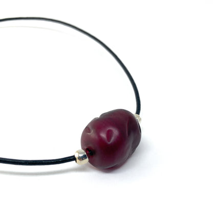 Black cord necklace with a dark red bead and silver accents.