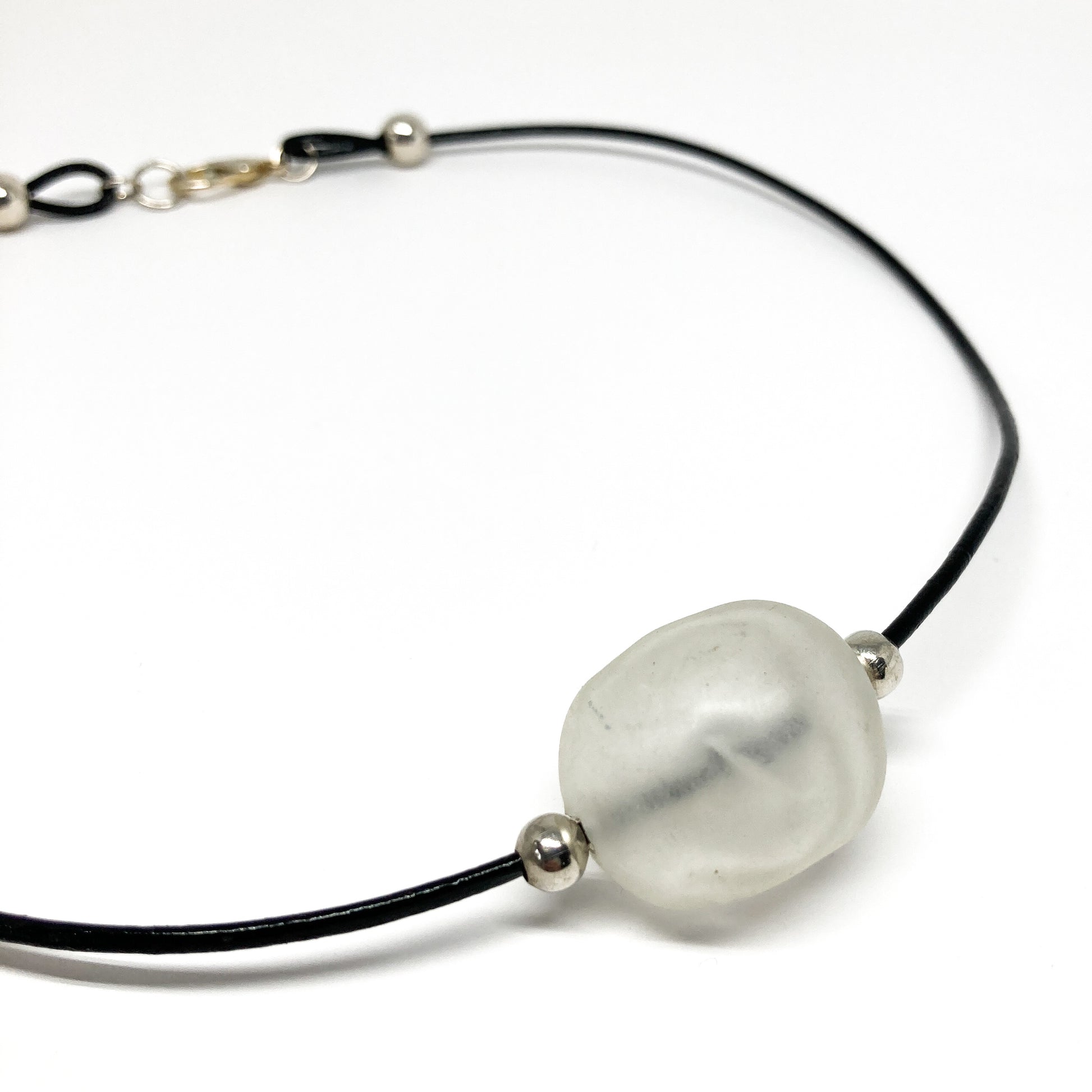 Black cord necklace with a light pink bead and silver accents.