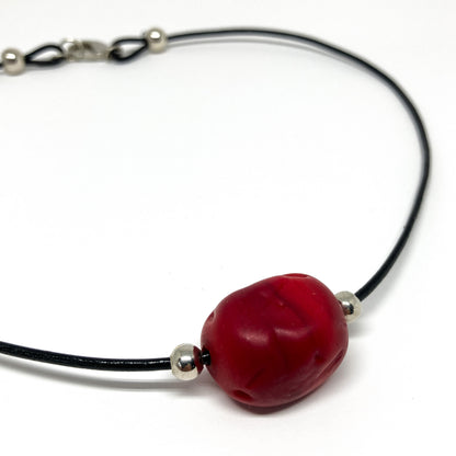 Black cord necklace with a red bead and silver accents.
