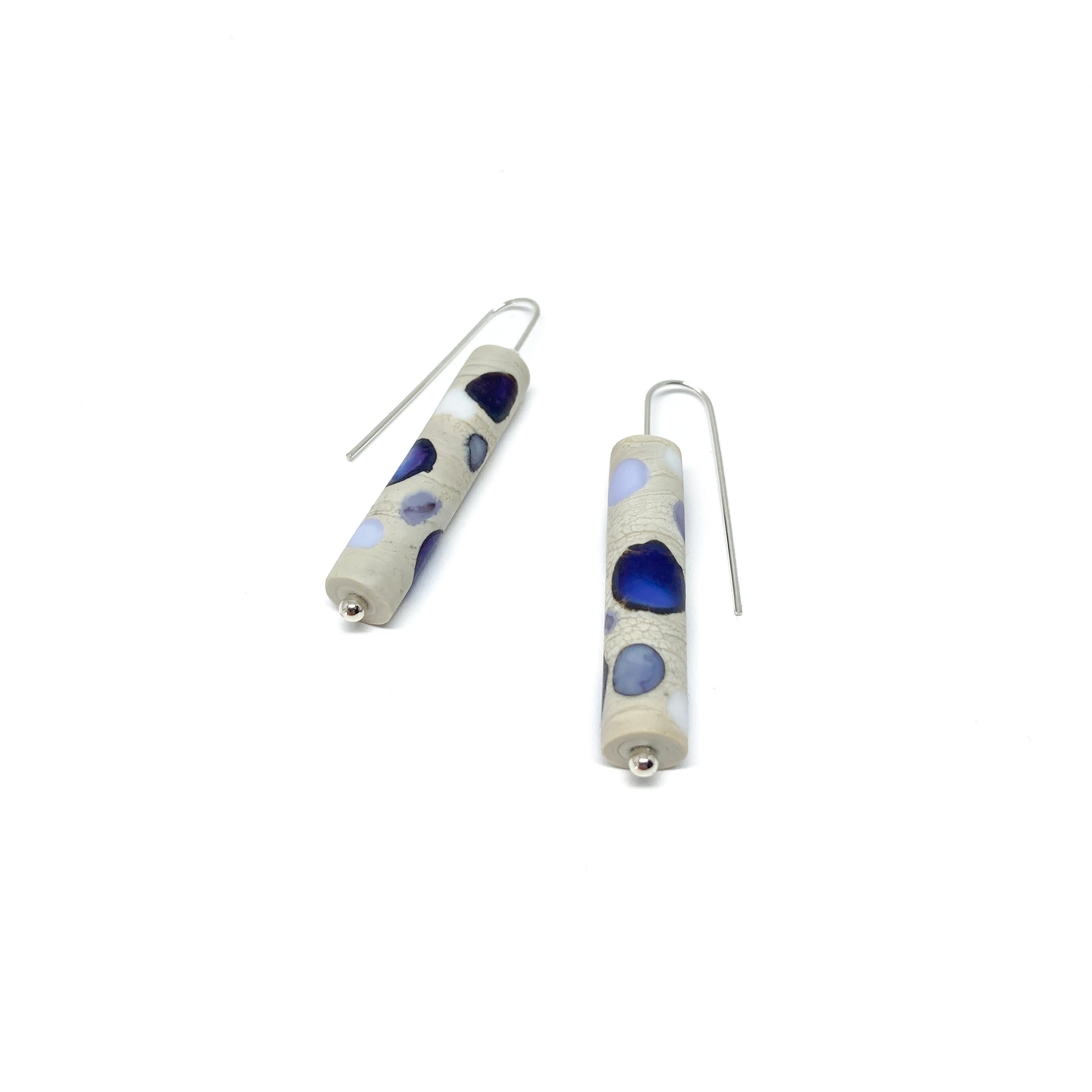 Two cylindrical earrings with purple, blue, and white dots, silver hooks, and small silver beads.