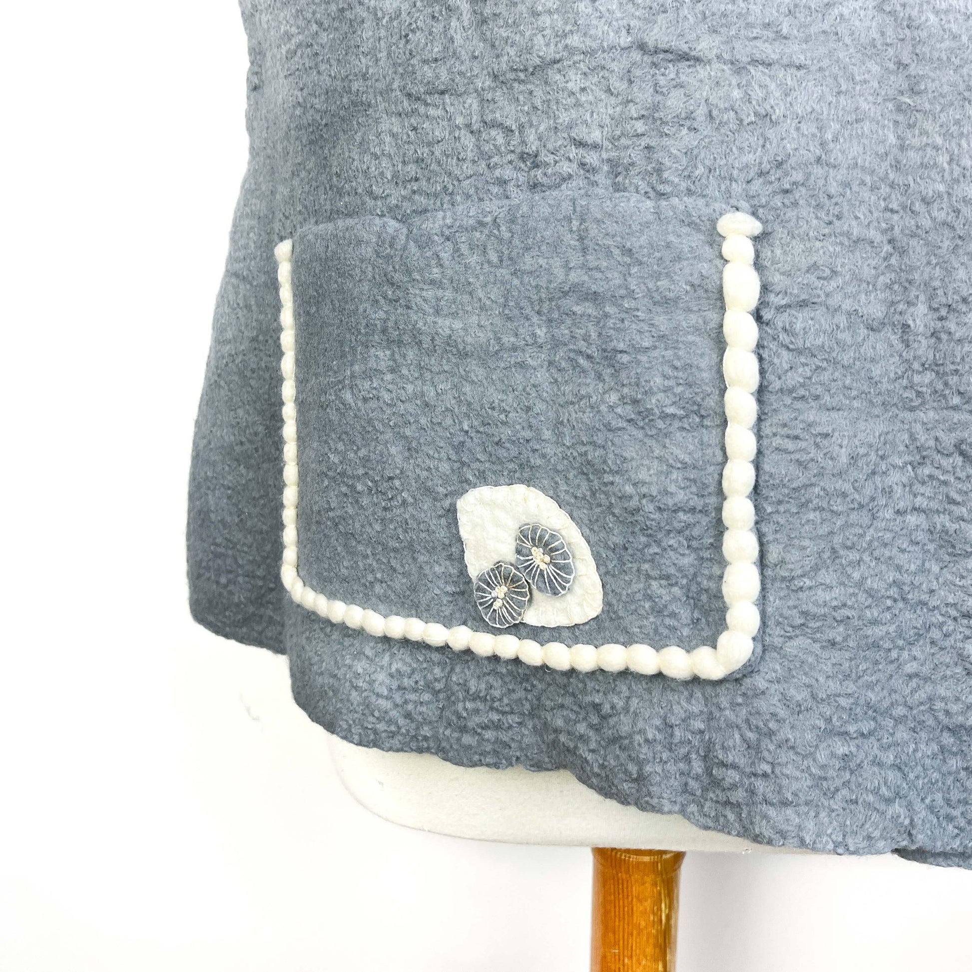 Detail of a gray Merino Wool Vest pocket with cotton yarn trim and decorative button.
