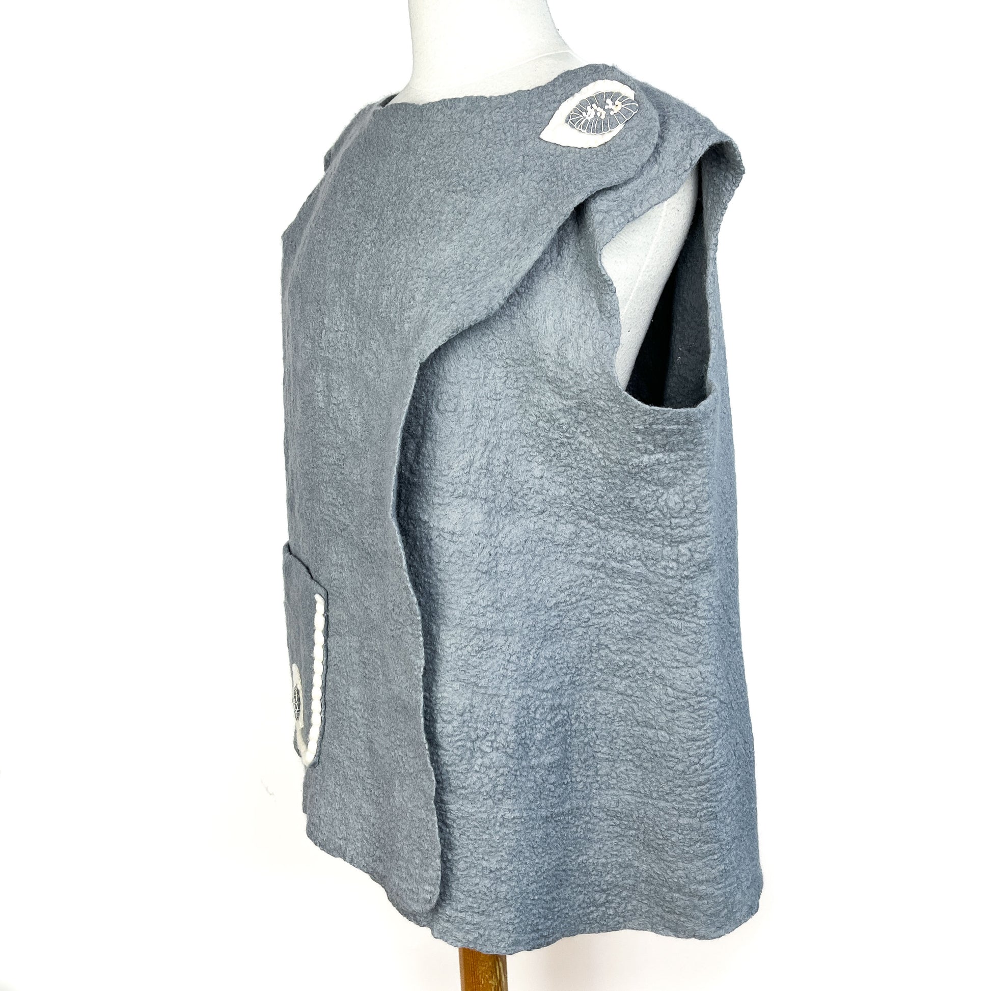 Side view of a gray Merino Wool Vest with cotton yarn detail on the pocket and shoulder.