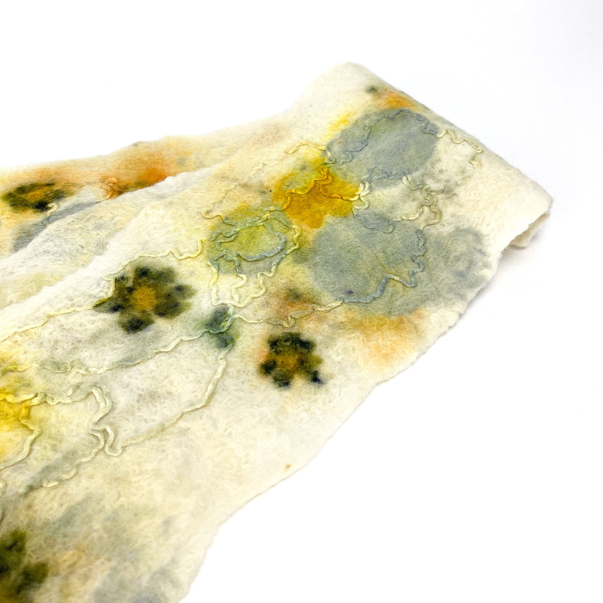 Close-up of an Eco Print Scarf. The off-white textile shows detailed imprints of leaves and flowers in soft yellow, green, and gray tones.