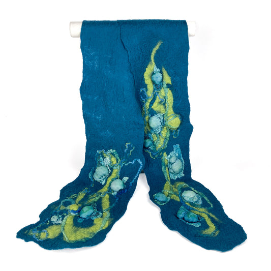 A flowing, textured Merino Ocean Scarf in deep teal with swirling accents of yellow, light blue, and white.