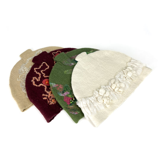 A row of four felted teapot cozies with unique floral and abstract embellishments.