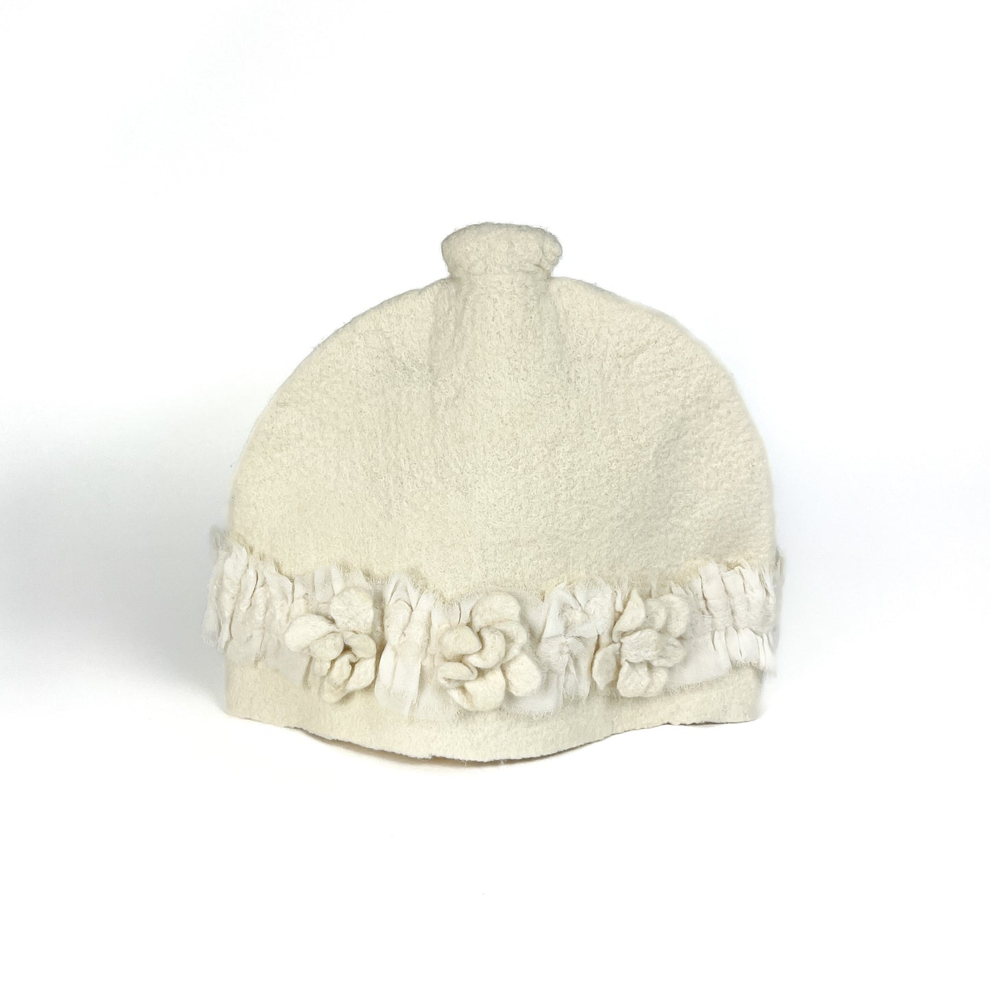 Off-white felted teapot cozie with textured floral appliqués and fringed detailing along the bottom.