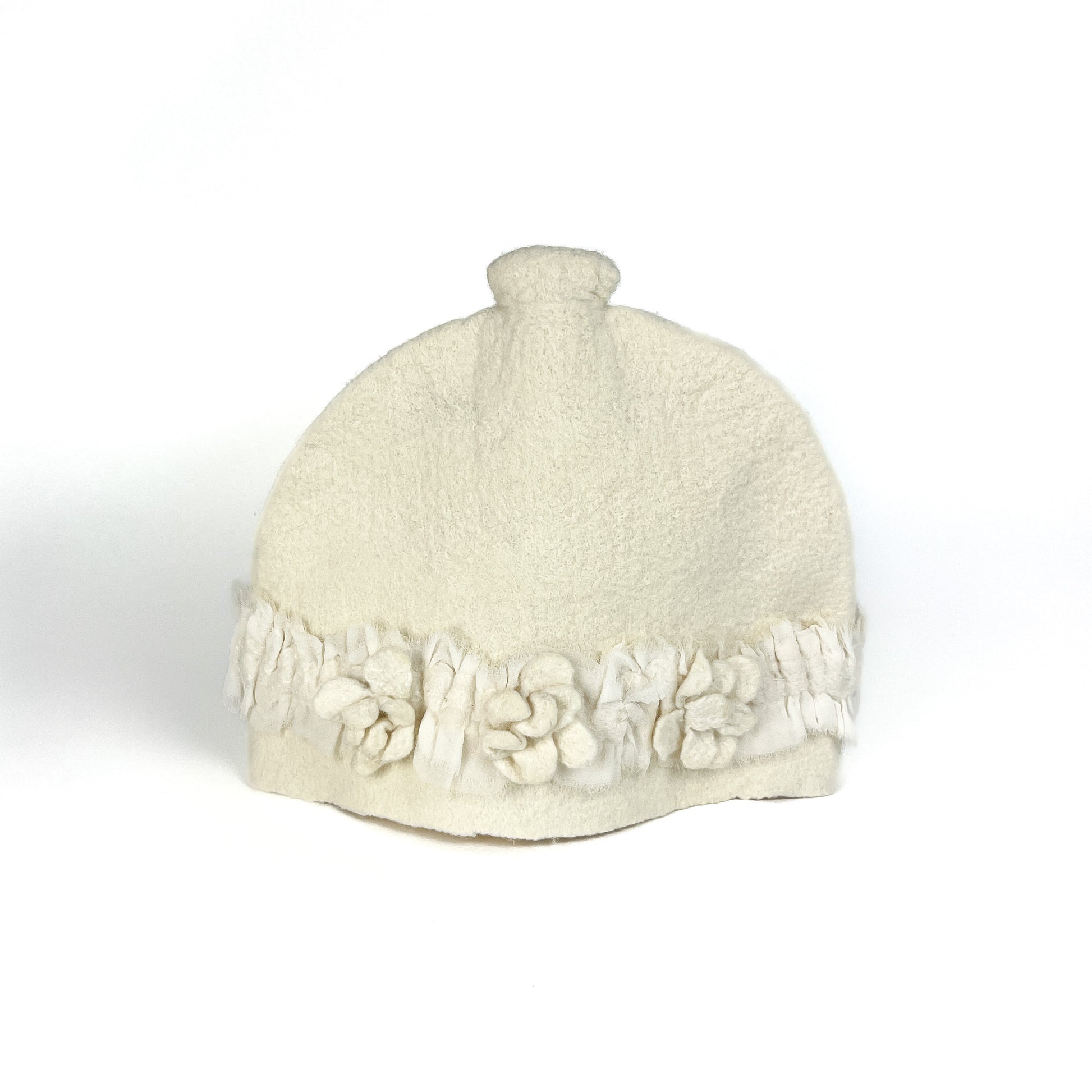 Off-white felted teapot cozie with textured floral appliqués and fringed detailing along the bottom.