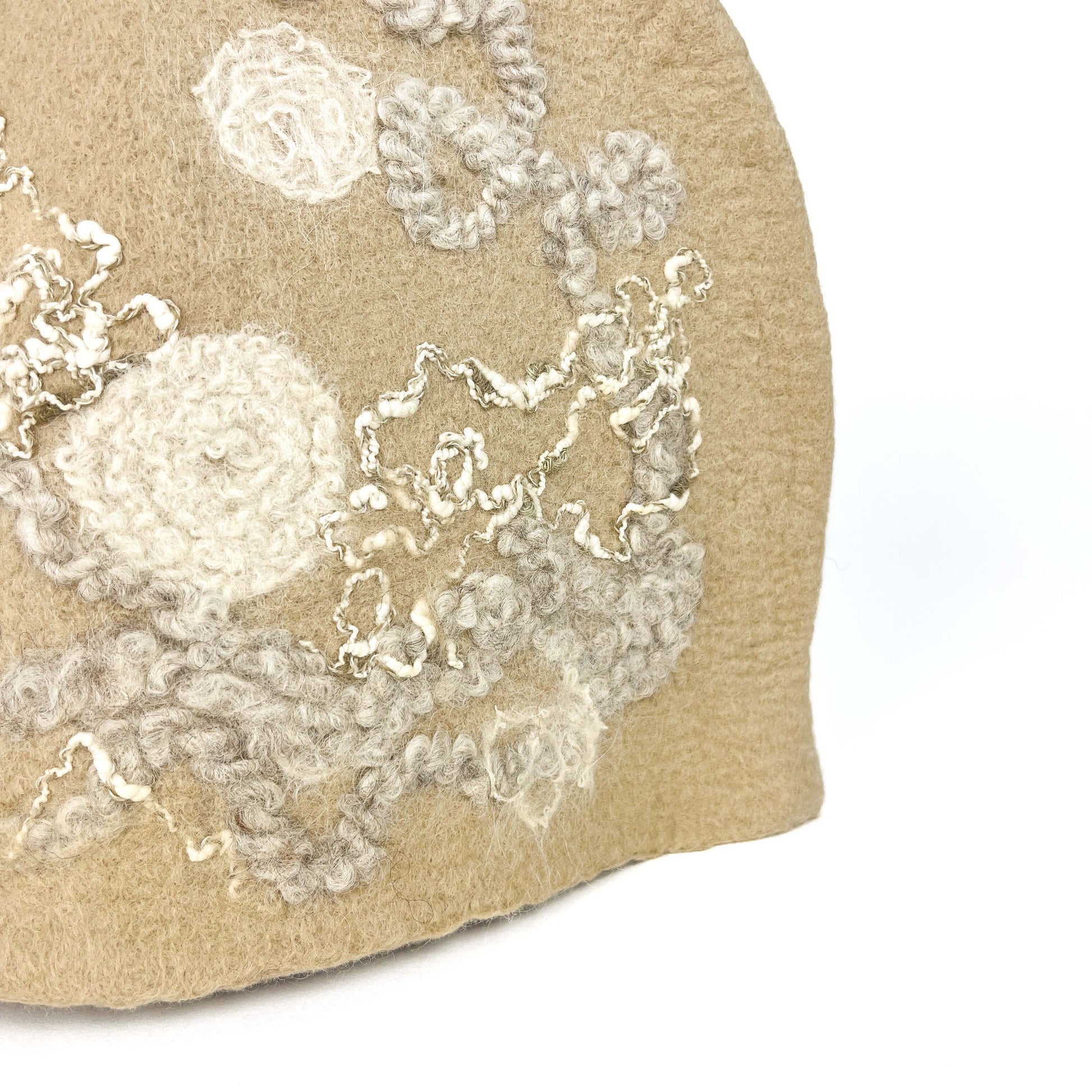 Close-up of a beige felted teapot cozie showing textured white and gray floral and abstract details.