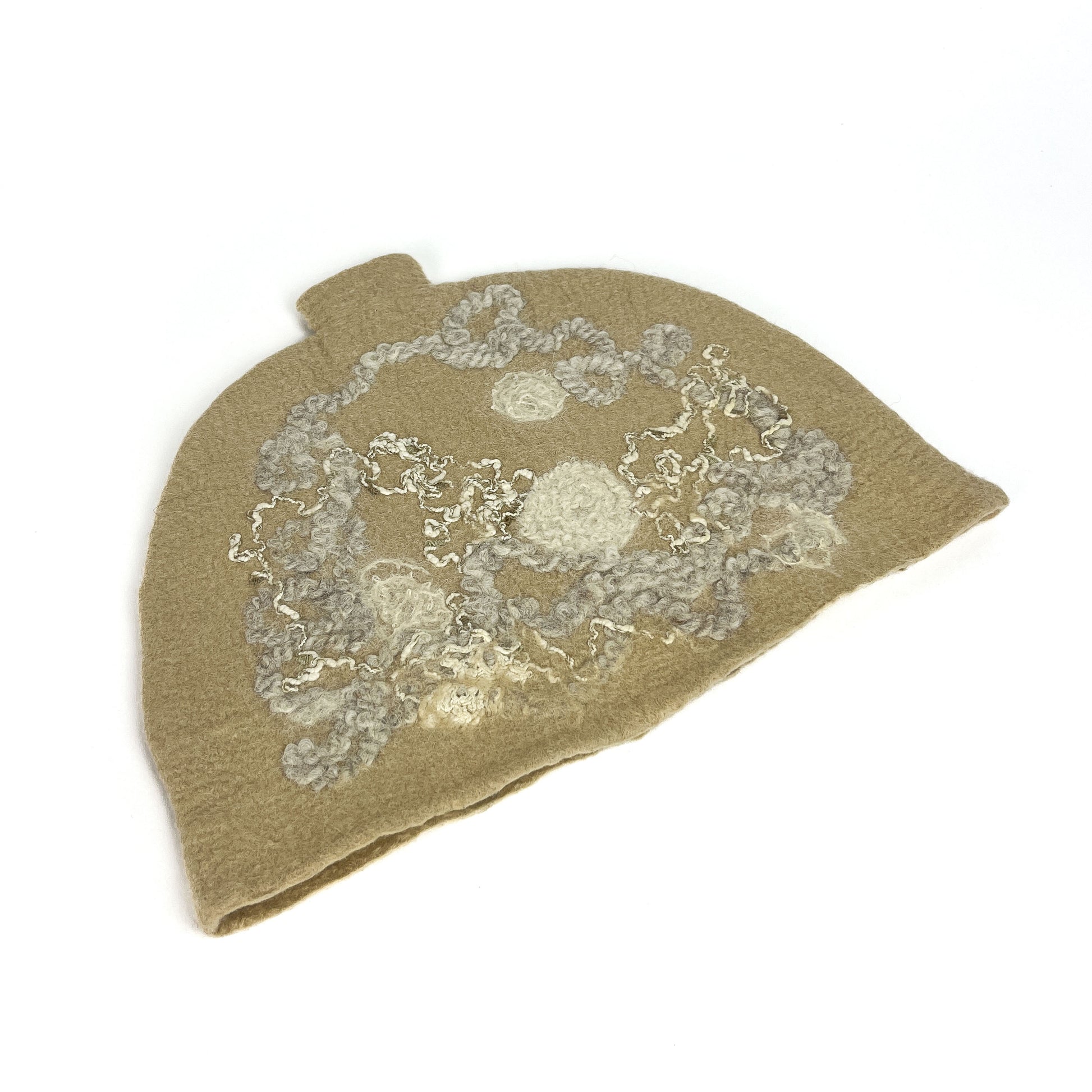 Angled view of a beige felted teapot cozie with textured white and gray abstract floral designs.