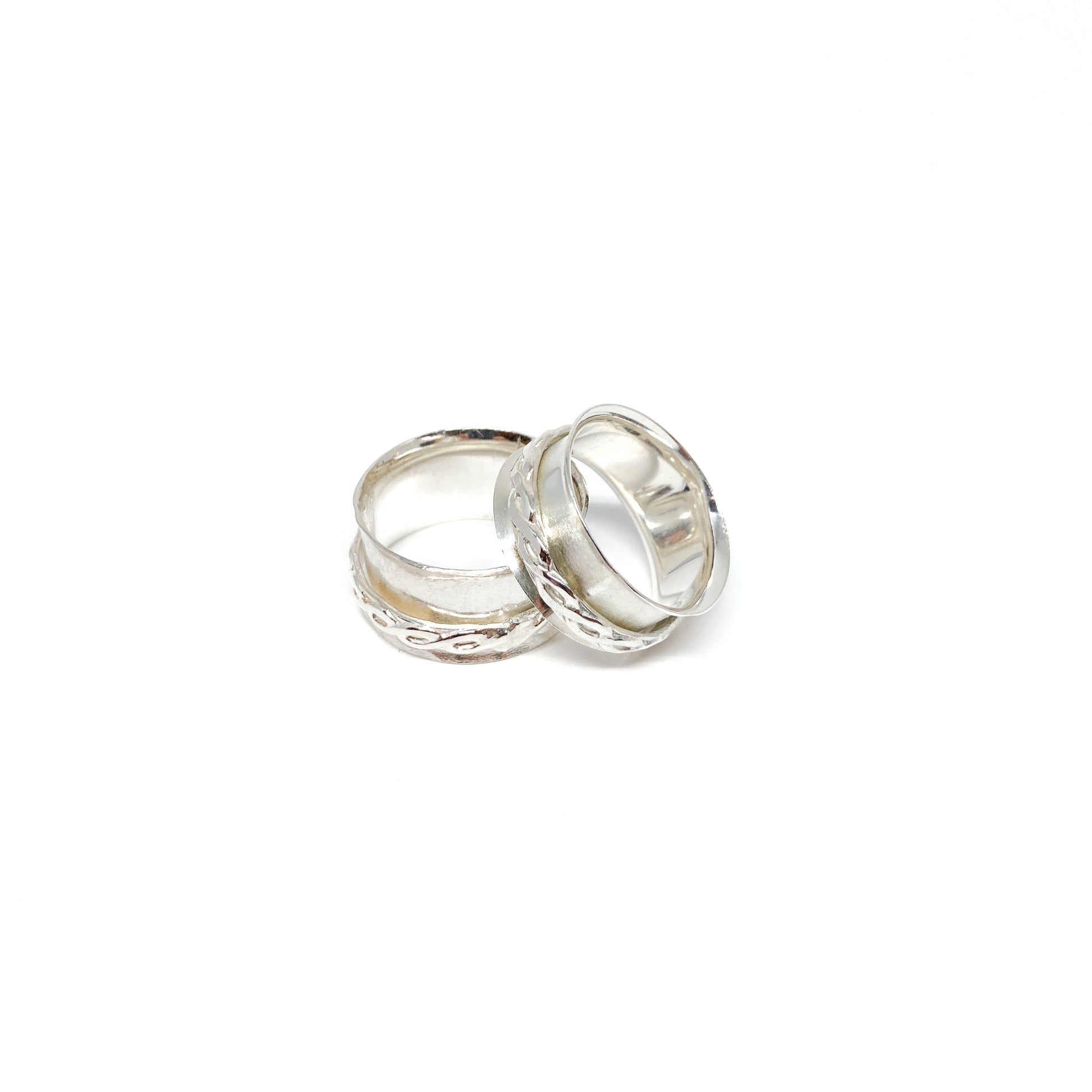 Two silver spinner rings with textured bands, one with a swirling pattern, resting on each other.