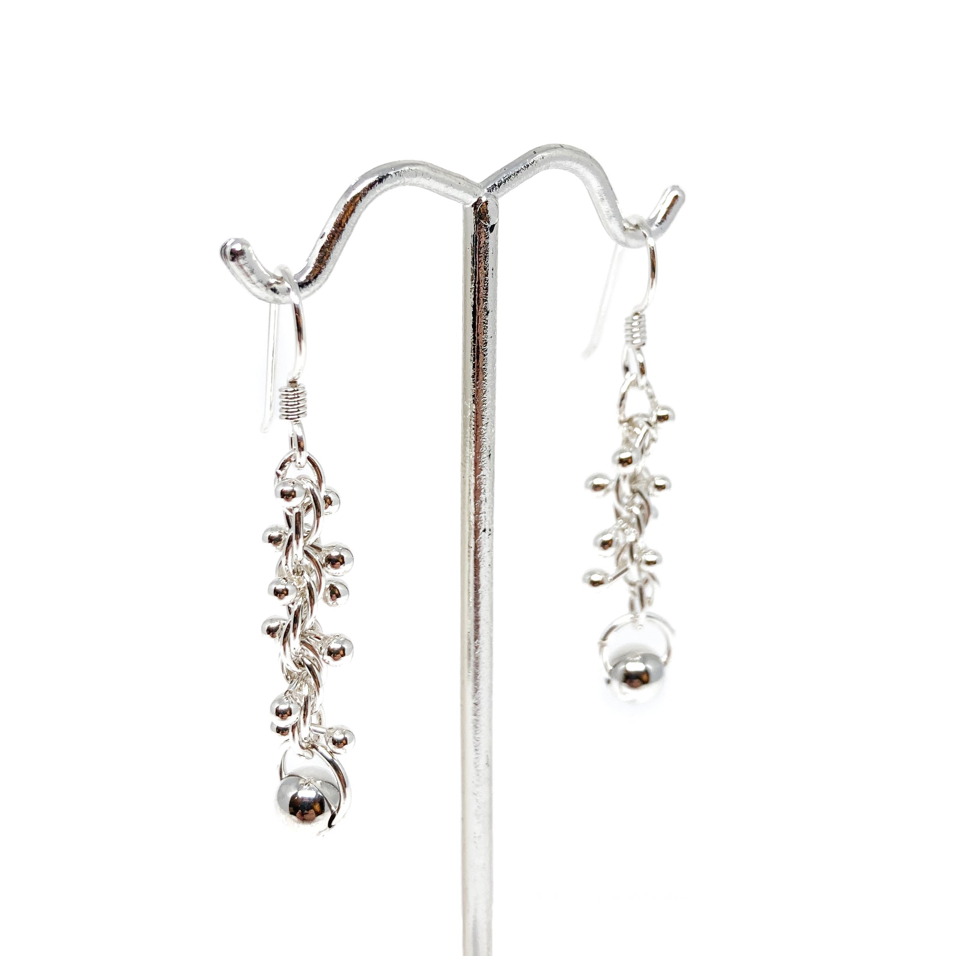 Baby Barbell Dangle Earrings displayed on a stand, showing clusters of silver balls and delicate chains.