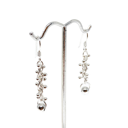 Baby Barbell Dangle Earrings displayed on a stand, showing clusters of silver balls and delicate chains.