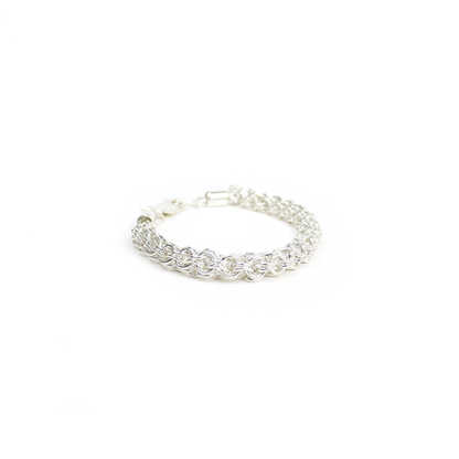Thick silver Chain Mail Bracelet placed on a wooden surface, showing intricate woven design.