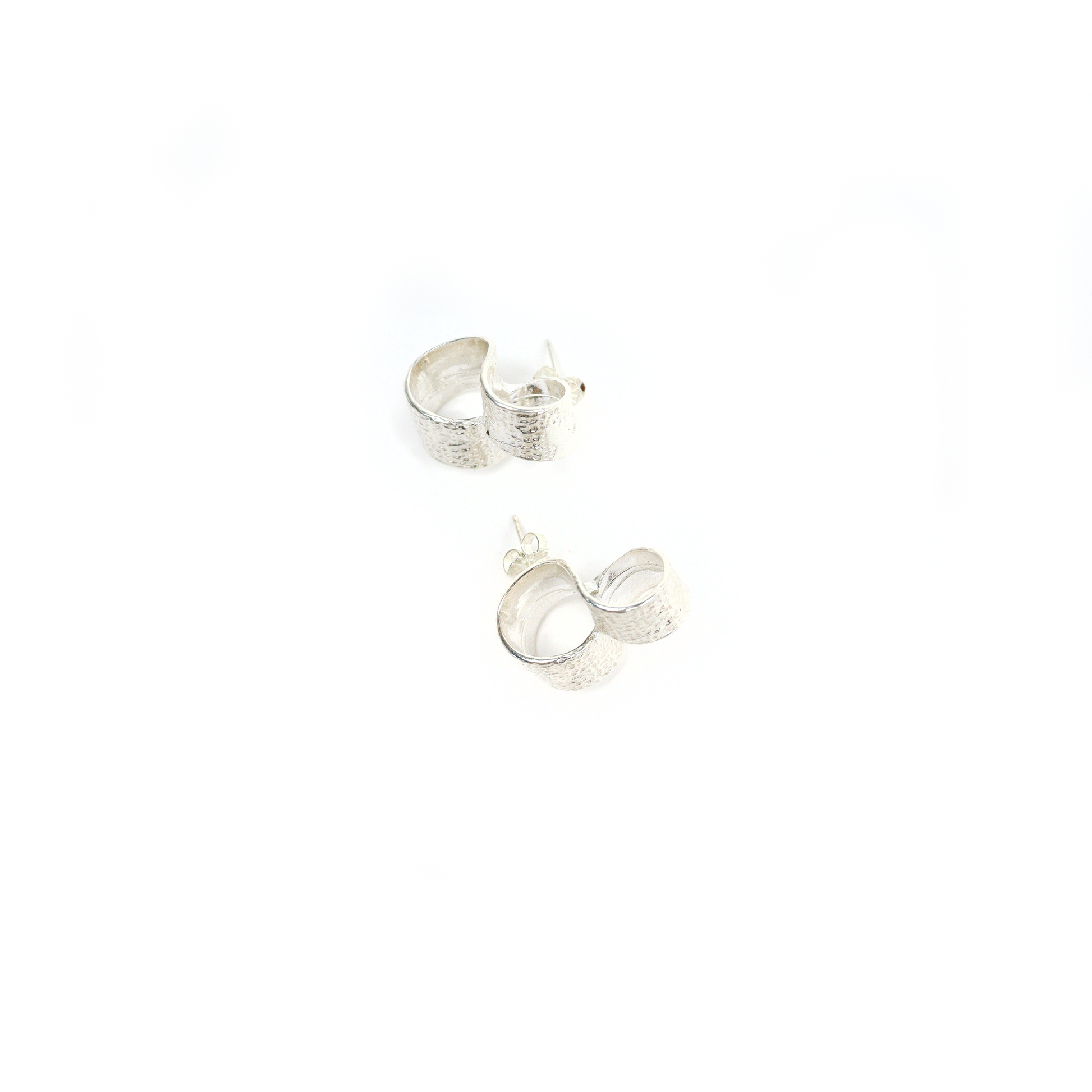 Close-up of New York Button Studs with textured silver surface and looped form, shown flat.