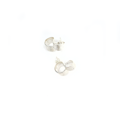 Close-up of New York Button Studs with textured silver surface and looped form, shown flat.