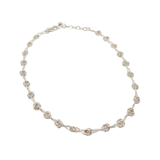 A delicate silver necklace featuring repeating infinity knot motifs along its chain.