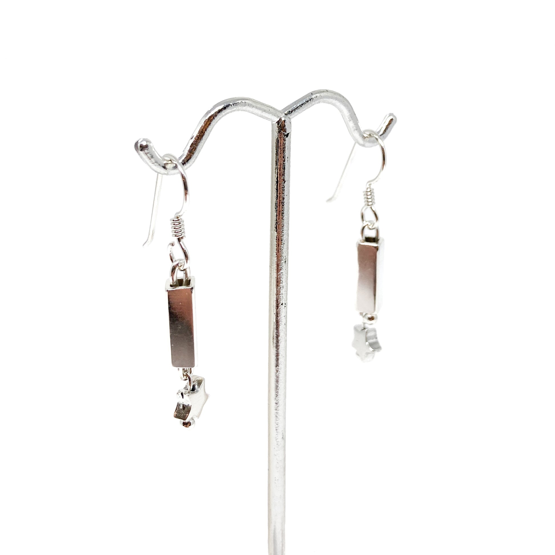 Silver earrings with square tubes and star charms displayed on a silver earring stand.