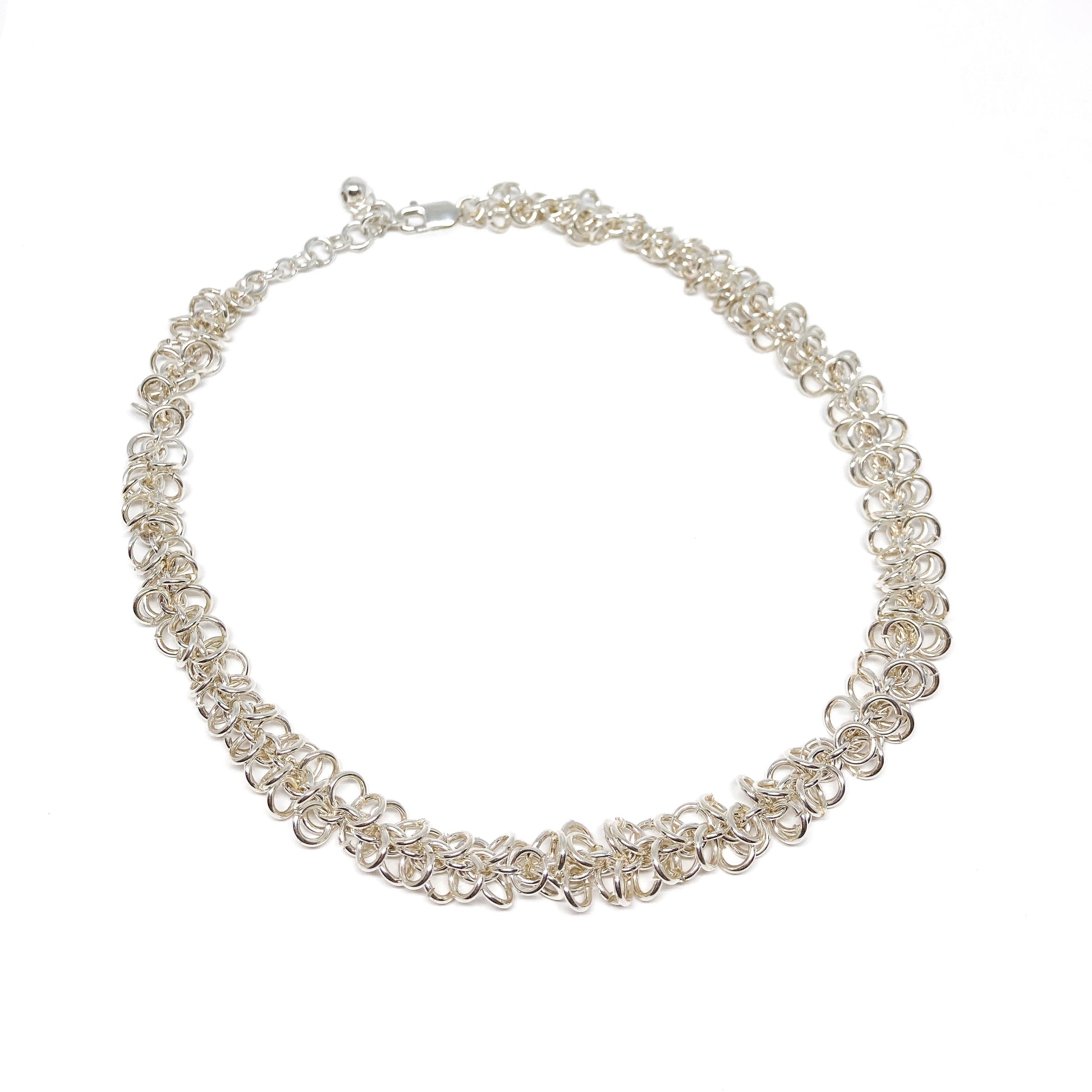 A shimmering silver Falling Link Necklace elegantly curves, showcasing its intricate chainmail-like design.