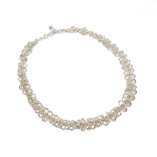 A shimmering silver Falling Link Necklace elegantly curves, showcasing its intricate chainmail-like design.